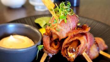 A plate with bacon-wrapped meat skewers, a small bowl of sauce, and a decorative garnish.