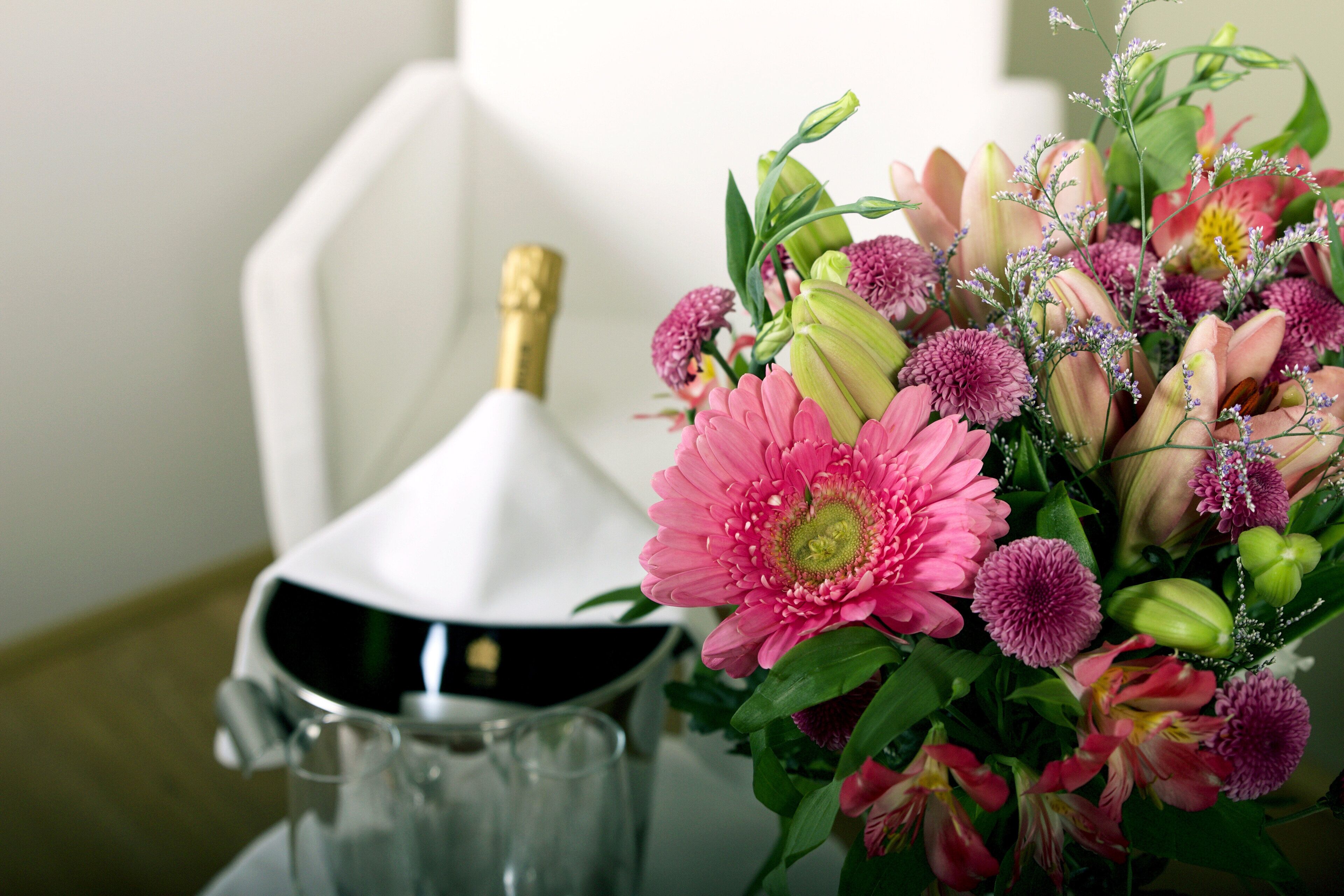 A table with a white vase containing a bouquet of flowers and a bottle of champagne.