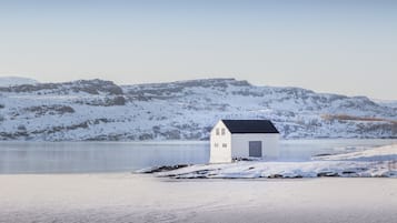 Ein kleines weißes Gebäude mit dunklem Dach in der Nähe eines ruhigen Sees, umgeben von schneebedeckten Hügeln.