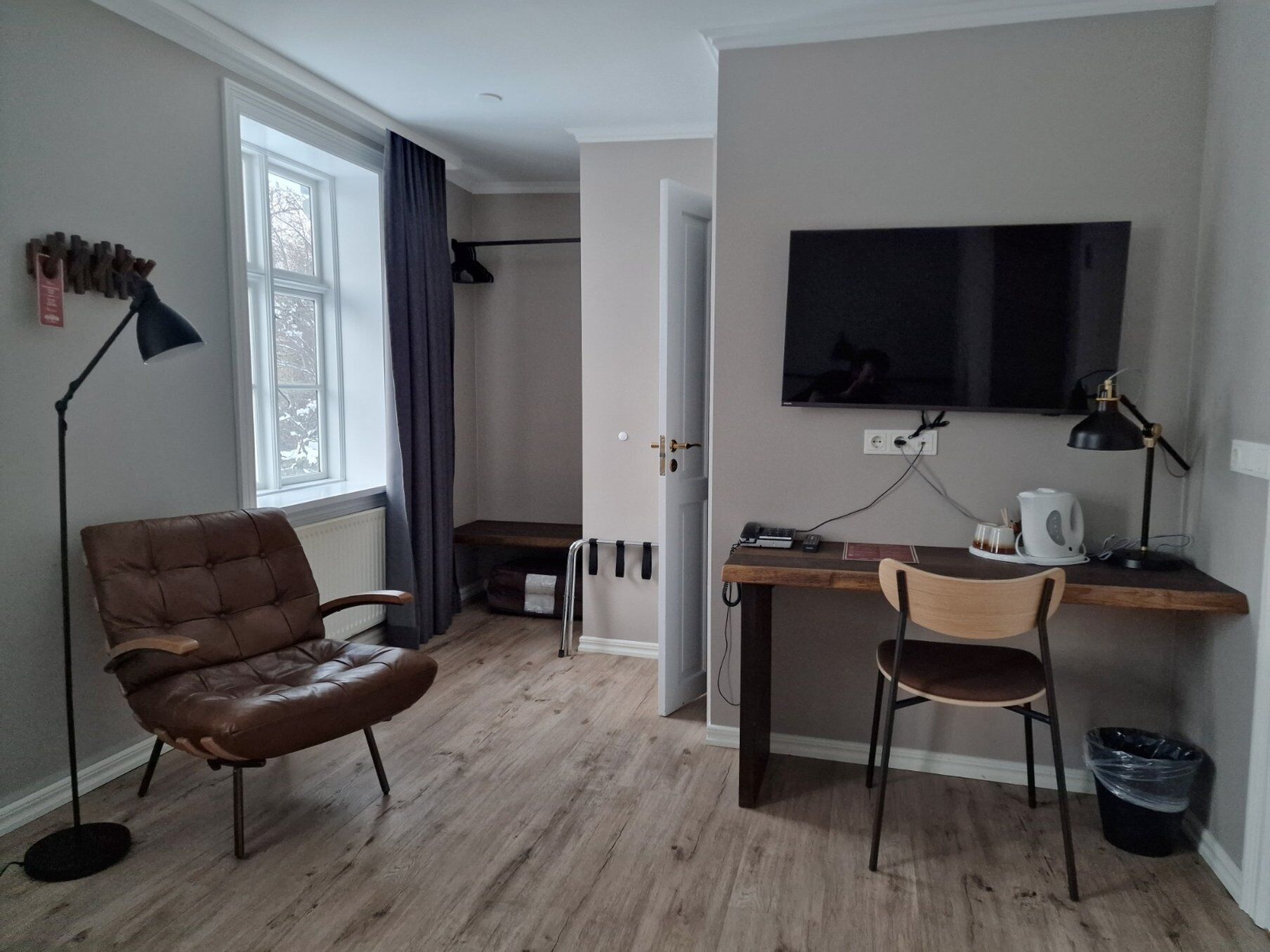 A compact room with a brown leather chair, a wooden desk, a television, and a small table with a coffee maker.