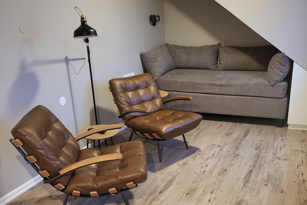 Una sala de estar moderna con un sofá de cuero marrón, dos sillones de cuero, una mesa de centro de madera y una lámpara de pie.
