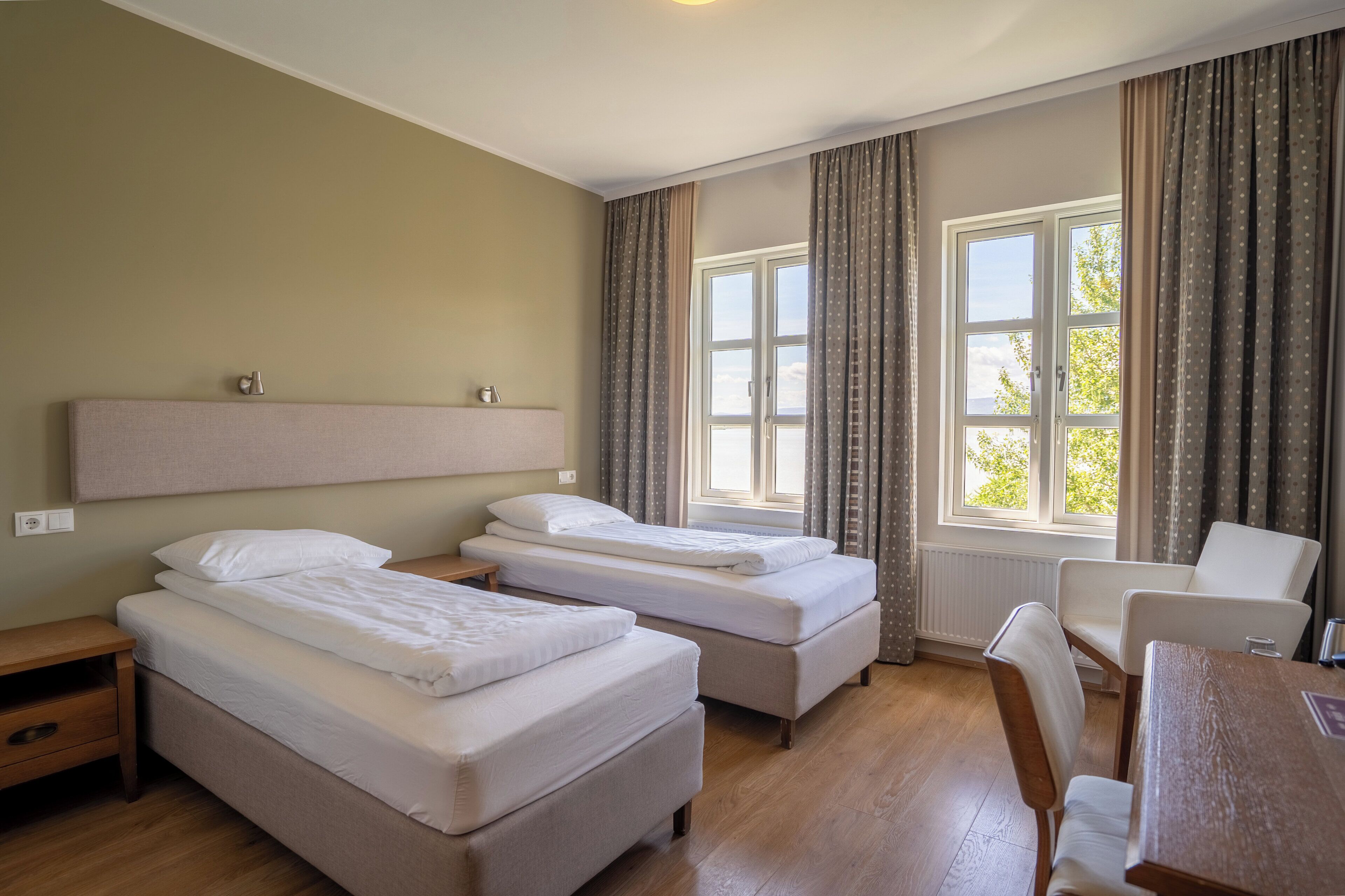 A hotel room with two single beds, a wooden desk, a chair, and a window with curtains.