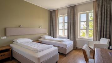 A hotel room with two single beds, a wooden desk, a chair, and a window with curtains.