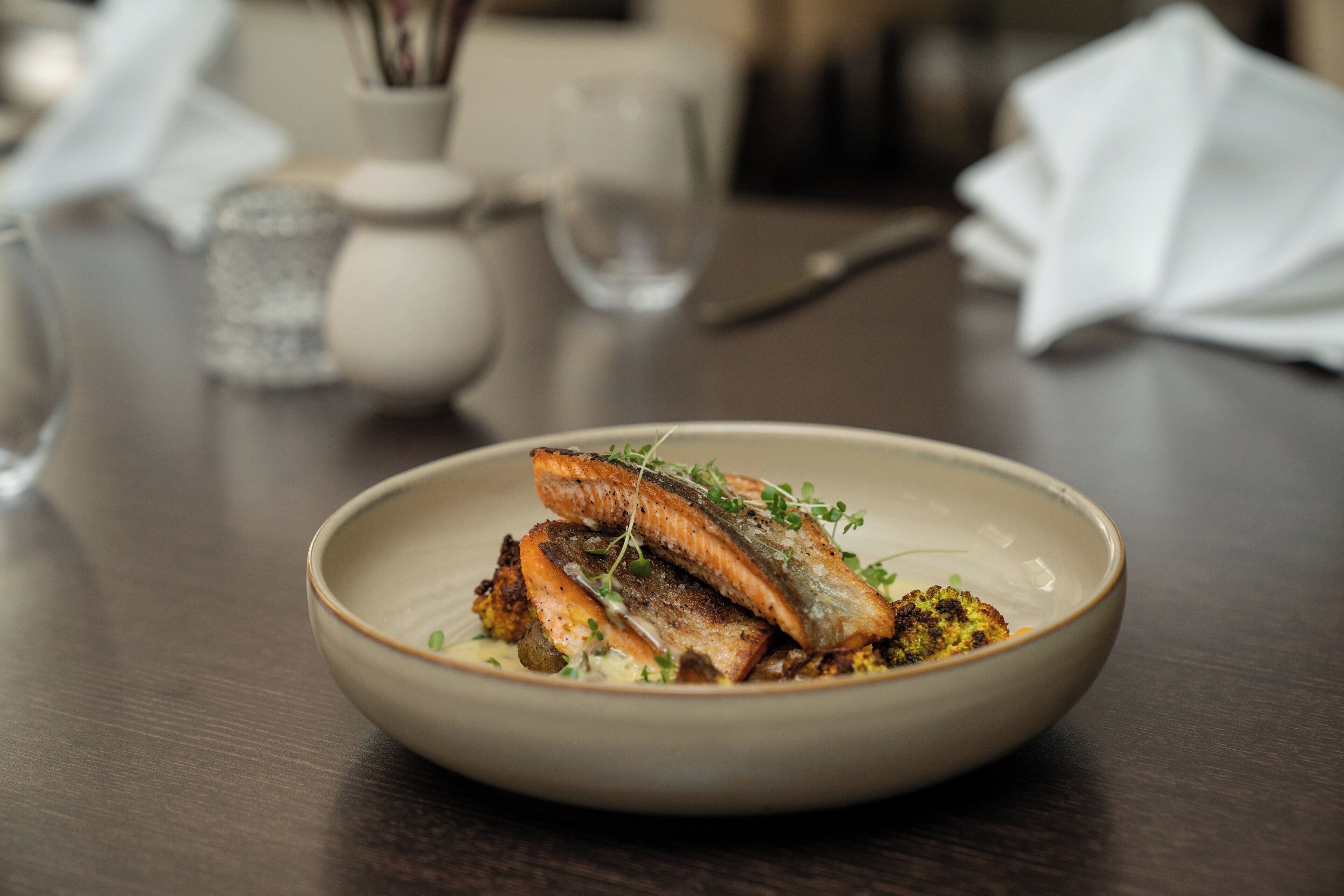 A bowl of food with salmon and greens on a wooden table.