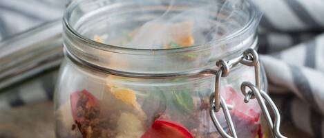 A glass jar with a metal clasp, containing various food items and emitting steam.