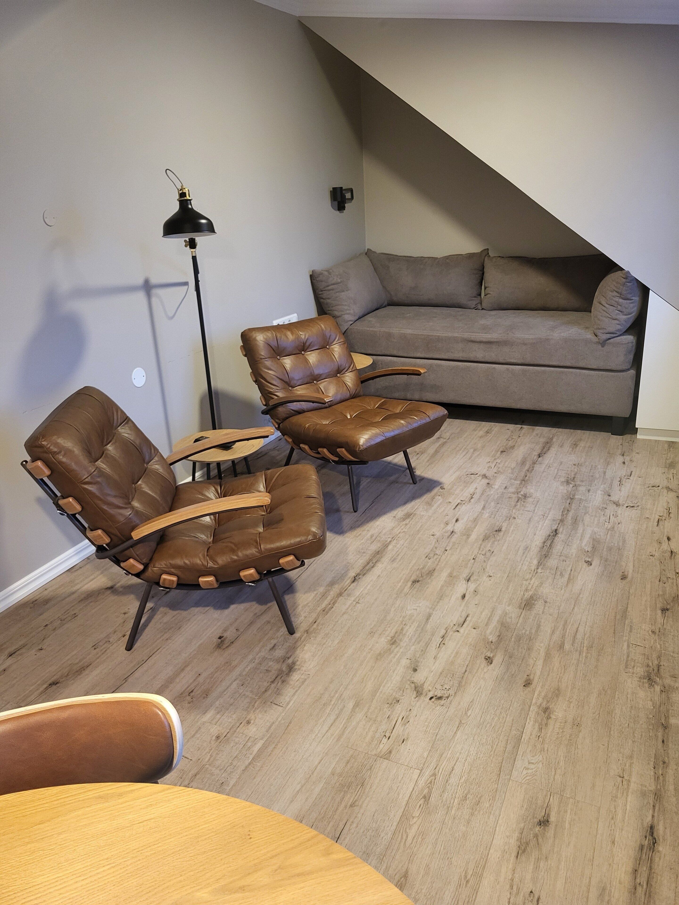 Ein Wohnzimmer mit einer braunen Ledersofa, zwei Ledersesseln, einem Holztisch und einer Stehlampe.
