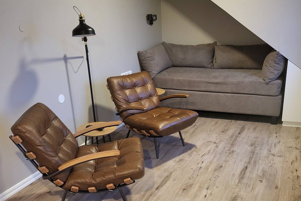 Una sala de estar moderna con un sofá de cuero marrón, dos sillones de cuero, una mesa de centro de madera y una lámpara de pie.