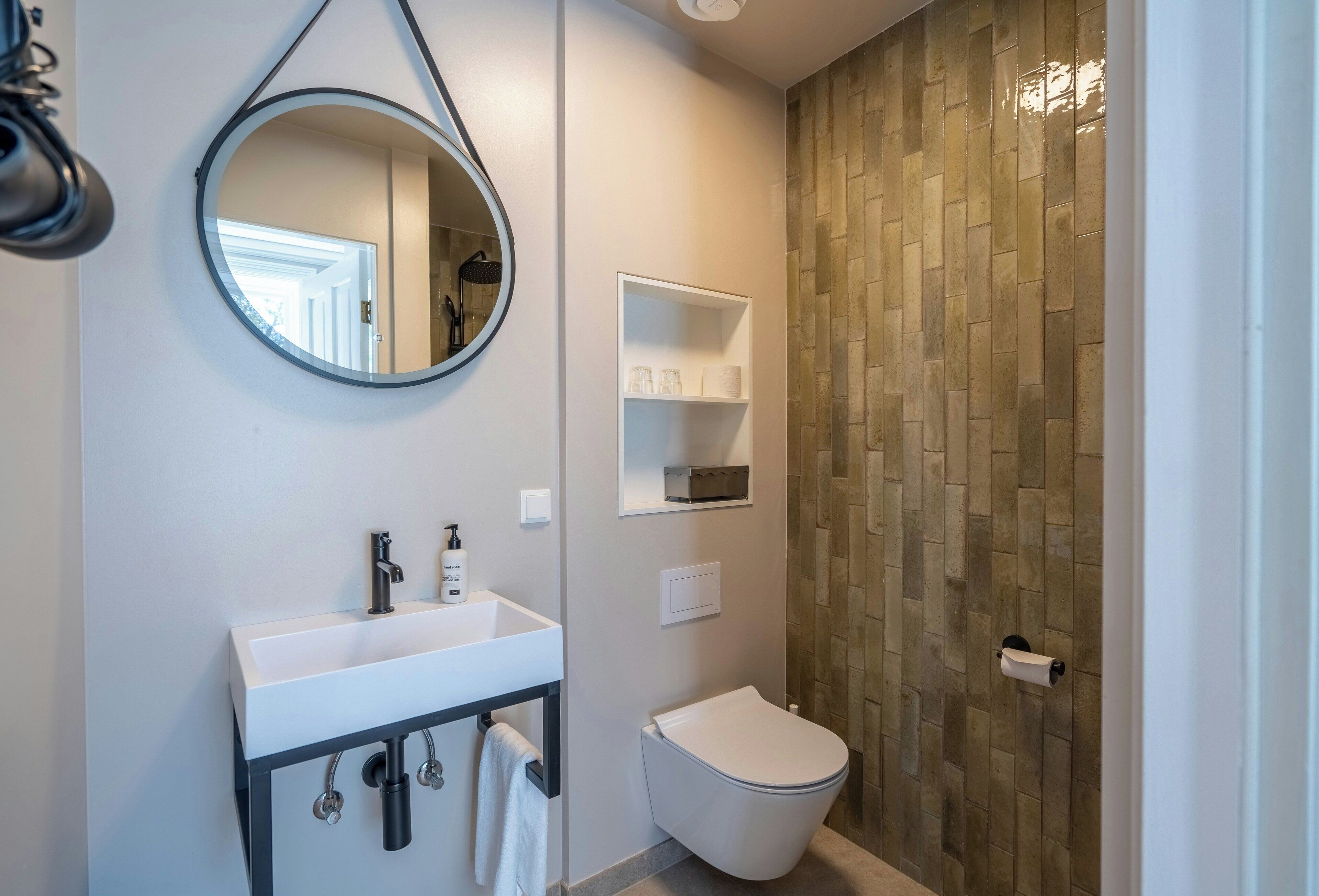 A modern bathroom with a white sink, a toilet, a mirror, and a shower area with a tiled wall.