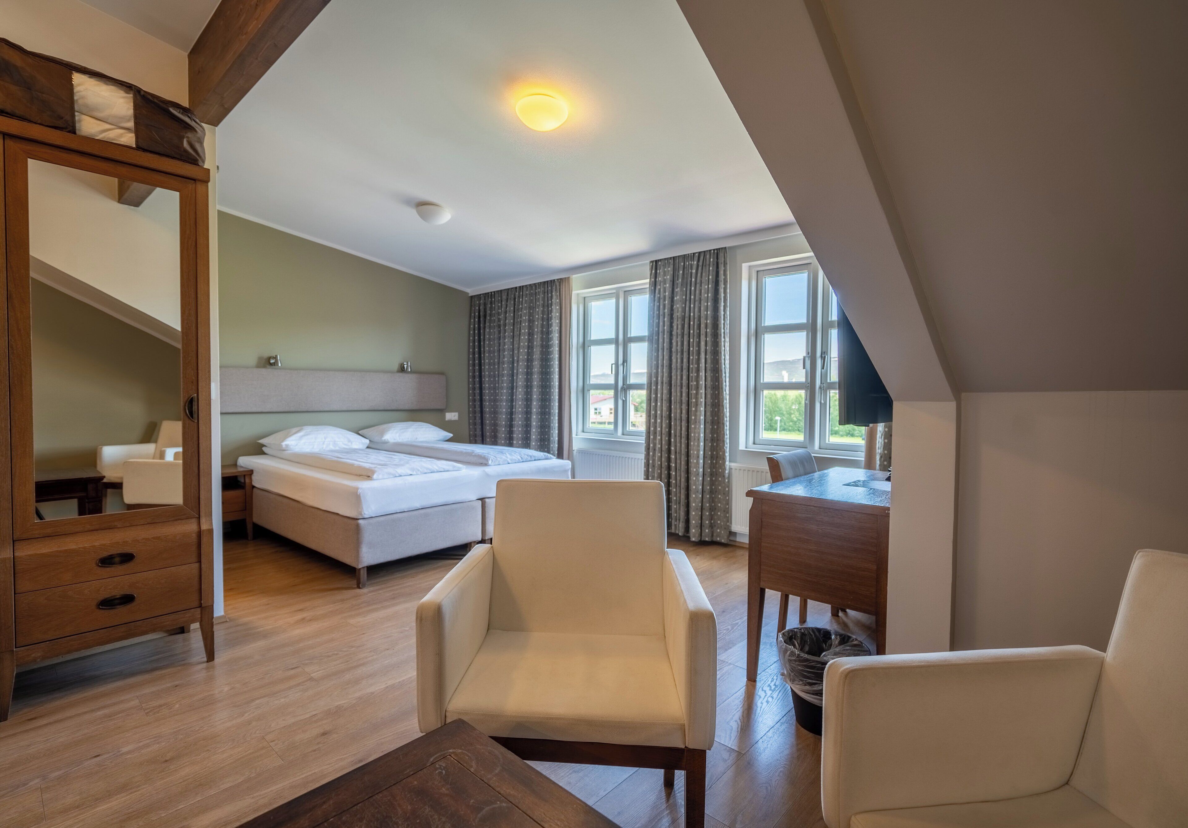 A bedroom with a bed, two chairs, a desk, a dresser, and a window with curtains.