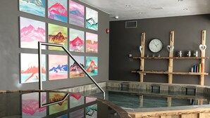 Un área de spa con un jacuzzi, repisas de madera con adornos y una pared con pinturas de montañas coloridas.