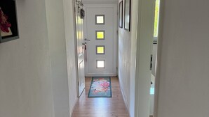 Un pasillo estrecho con suelo de madera, un tapete floral y una puerta con cuatro paneles iluminados.