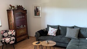 Una sala de estar con sofá, una mesa de centro de madera, un sillón estampado, un aparador antiguo y un cuadro en la pared.