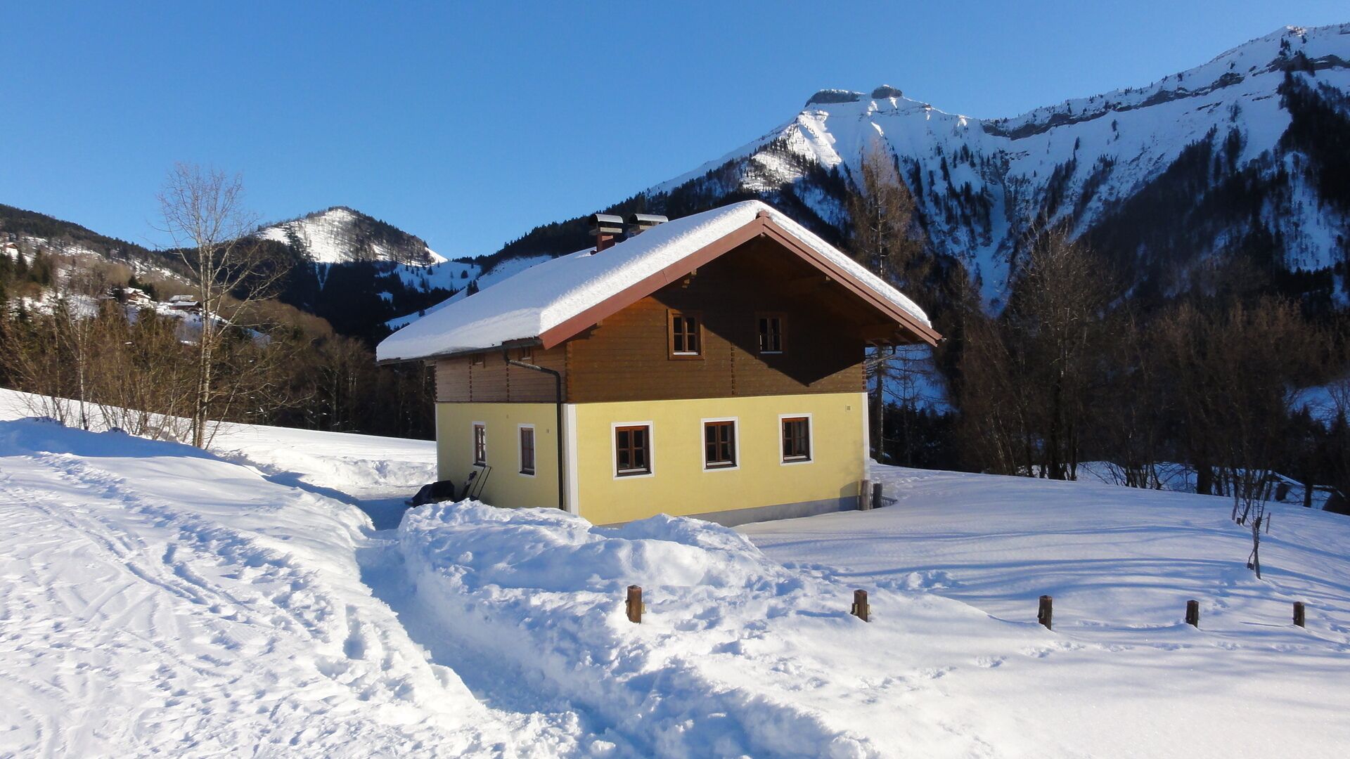 A small, two-story chalet with a sloped roof, situated in a snowy mountainous area.