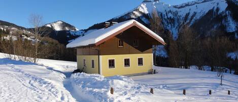 A small, two-story chalet with a sloped roof, situated in a snowy mountainous area.