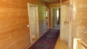 A wooden interior hallway with open doors leading to other rooms, a patterned rug on the floor, and a wooden bench at the end.