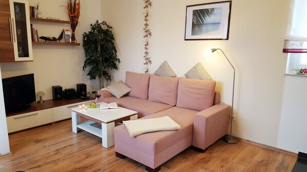 A modern living room with a pink sofa, a white coffee table, and a television.