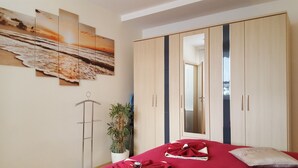 A bedroom with a bed, a wardrobe, a mirror, and a wall with three paintings.