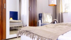 Una habitación de hotel con cama, una silla, una lámpara y un armario.