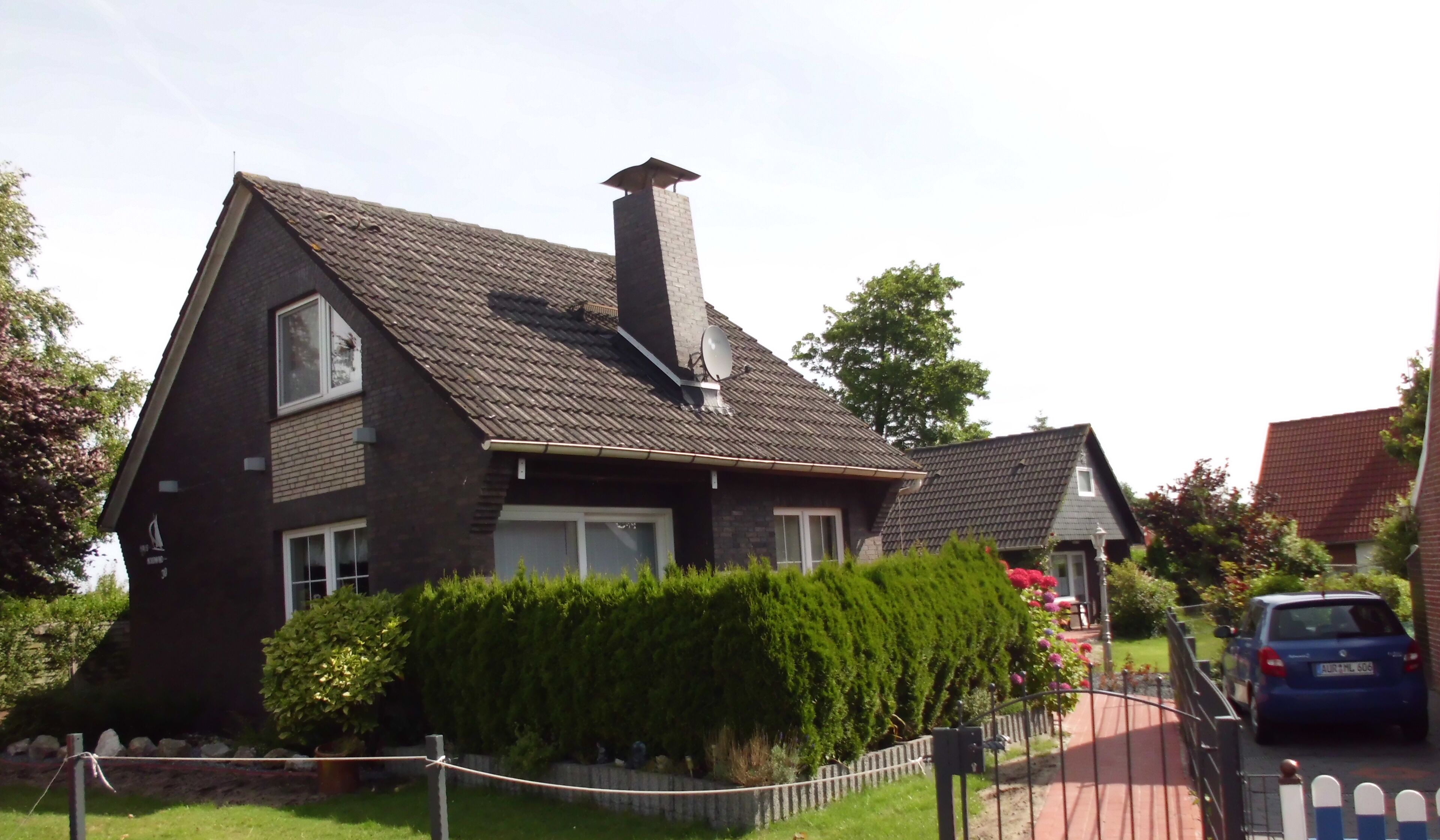 A two-story house with a steeply pitched roof, a chimney, and a satellite dish.