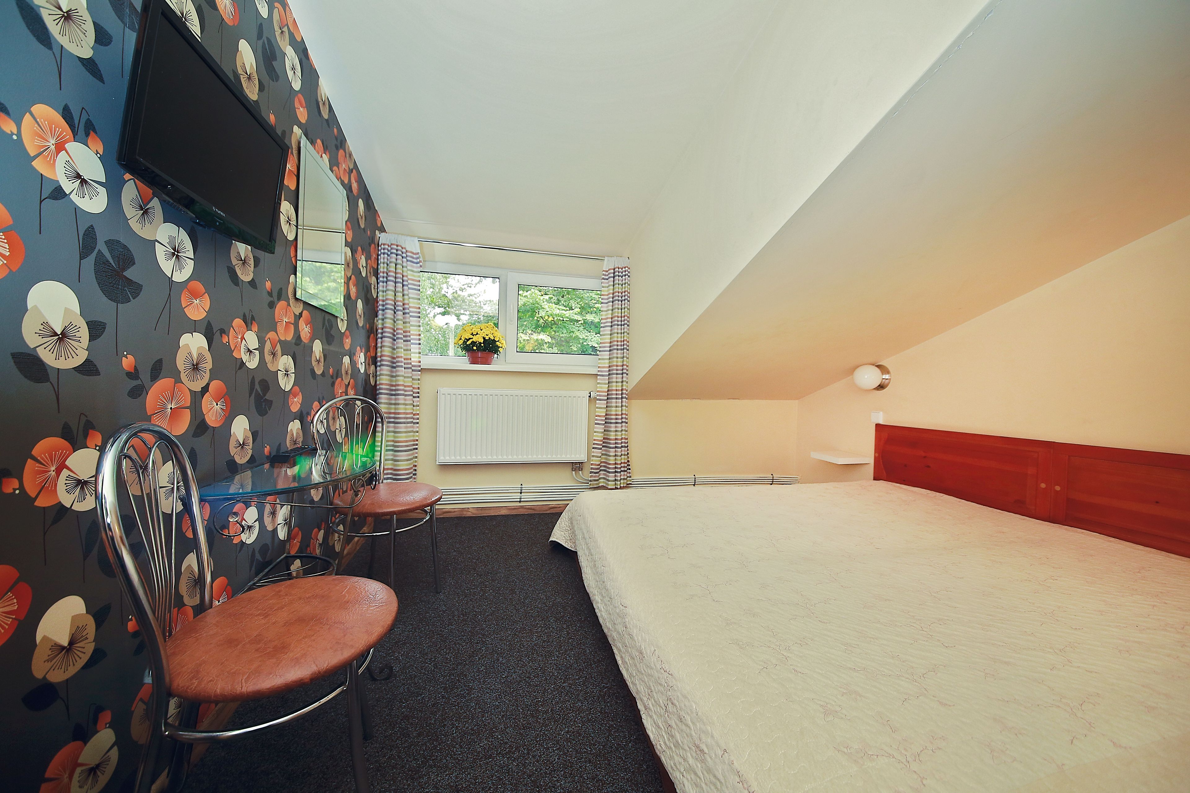 A bedroom with a bed, a desk, two chairs, a TV, and a window with curtains.