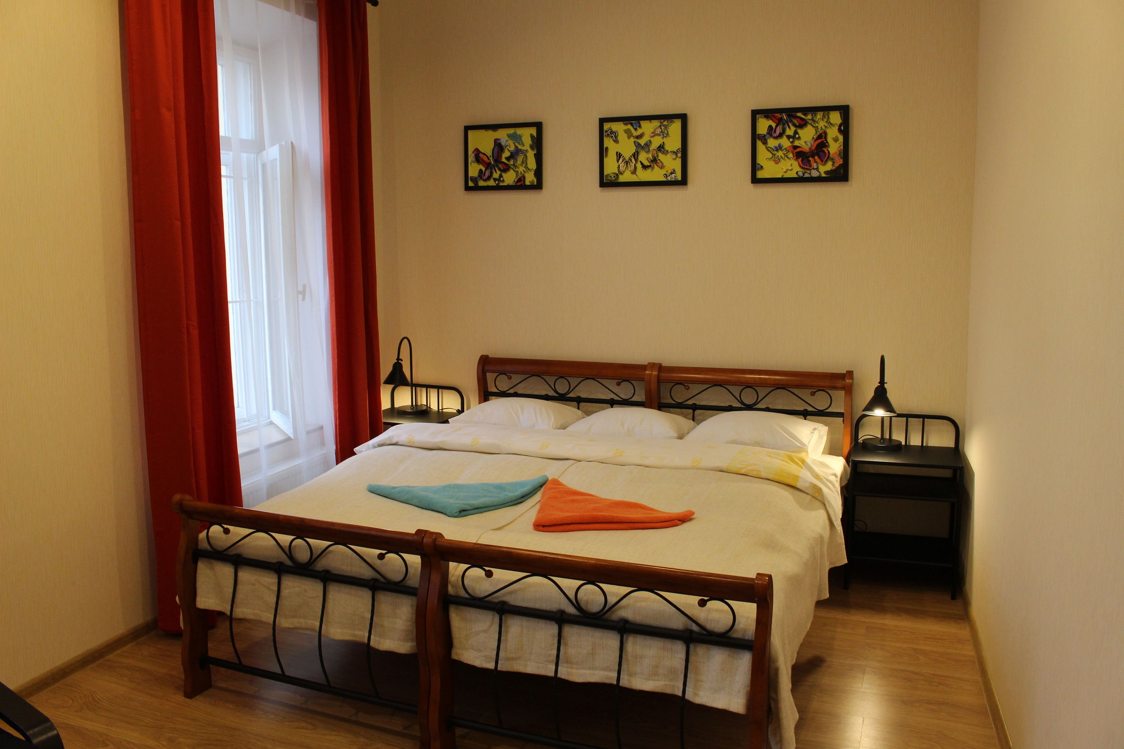 A neatly made bed with a wooden frame, a bedside table with a lamp, and three butterfly-themed wall art pieces.