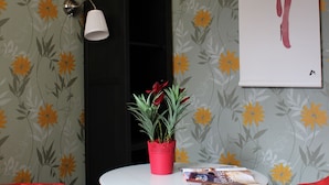 A room with floral wallpaper, a black cabinet, a white table with a magazine, and red bean bags. - Sleep In BnB (Vilnius)