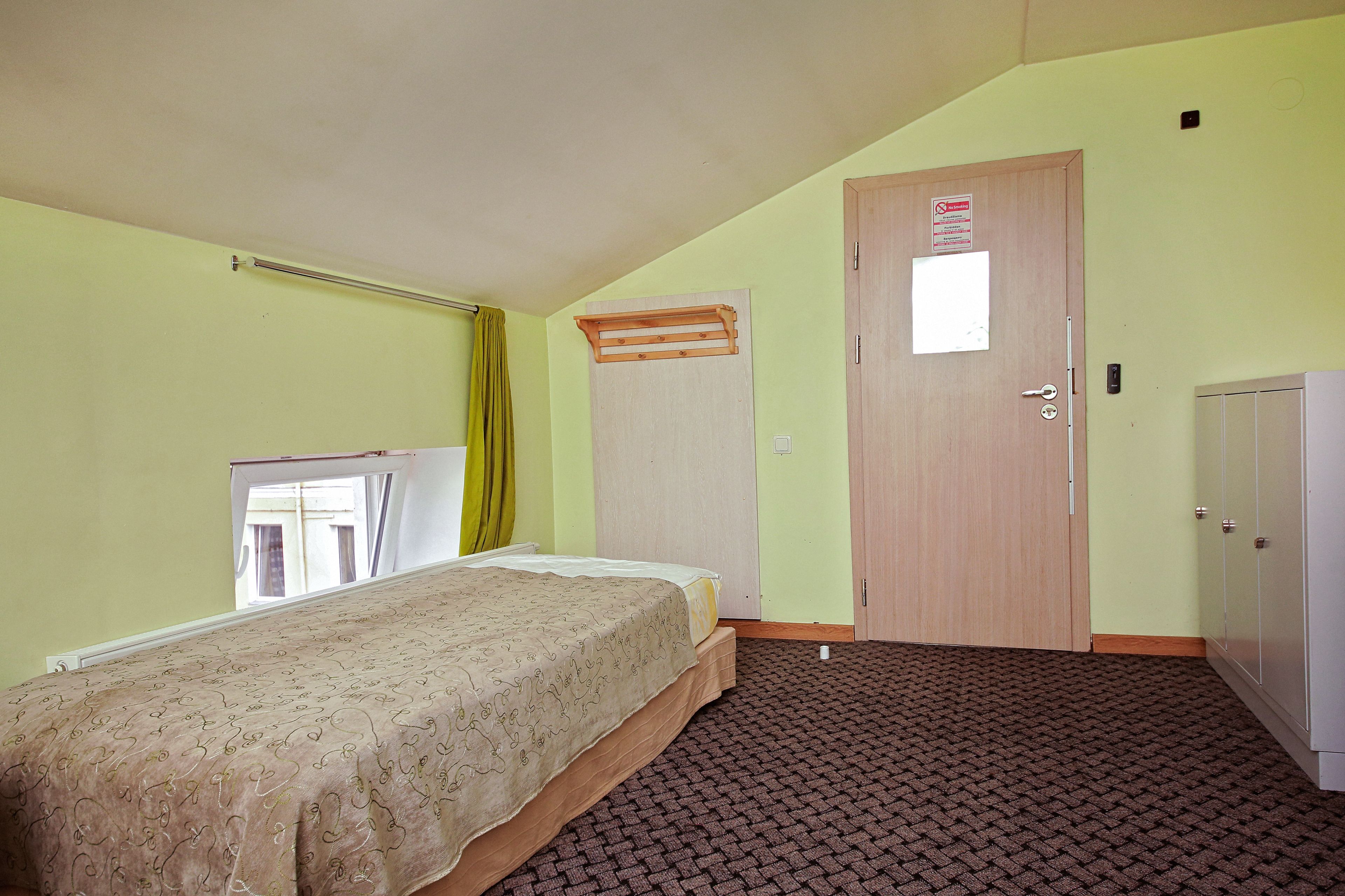 A room with a bed, a wardrobe, a door with a sign, and a window with curtains.