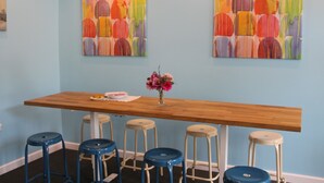 A bar area with a wooden counter, blue stools, and two colorful abstract paintings on the wall. - Sleep In BnB (Vilnius)