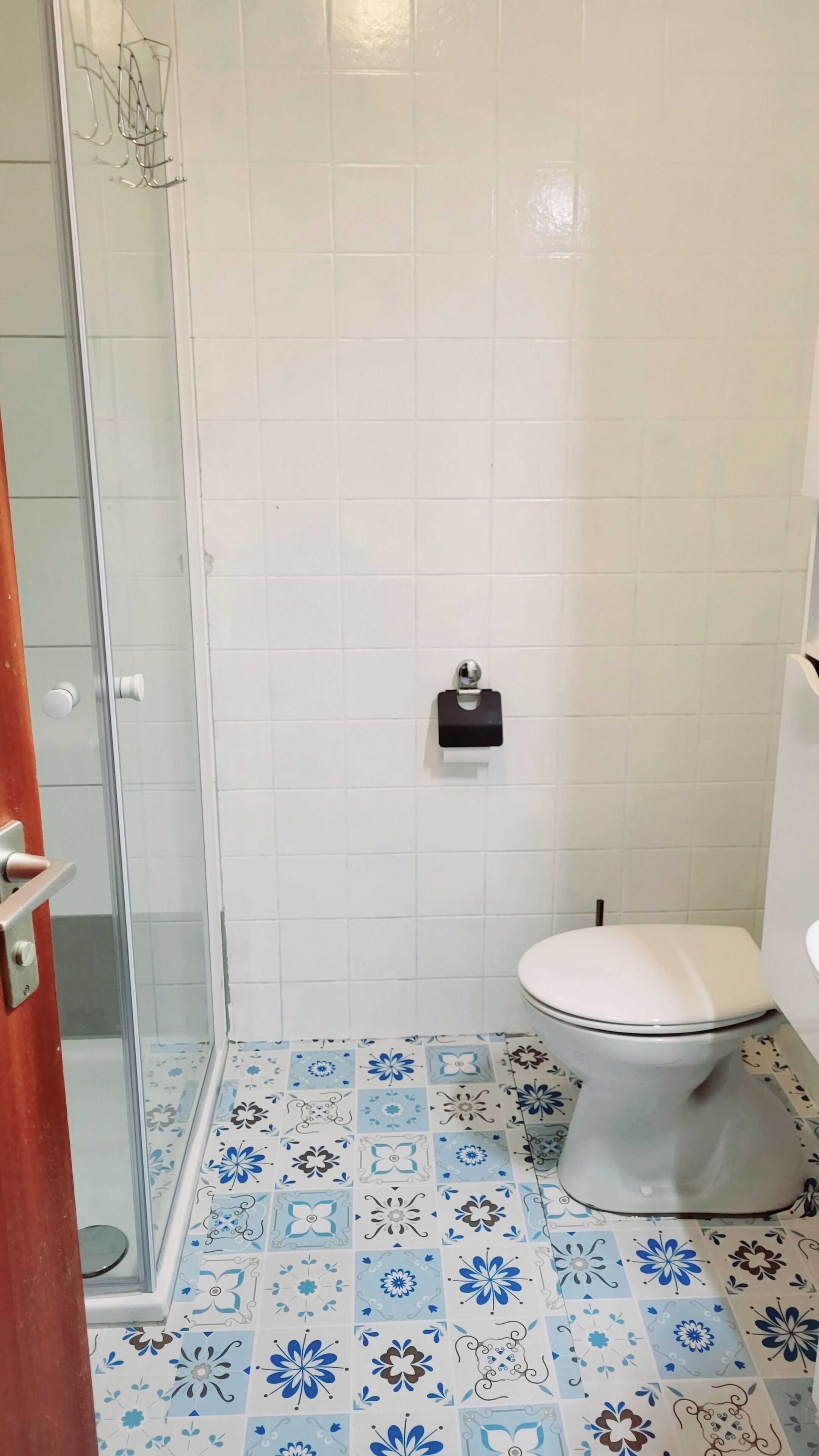 Un baño con inodoro, cabina de ducha de vidrio y baldosas de suelo estampadas.