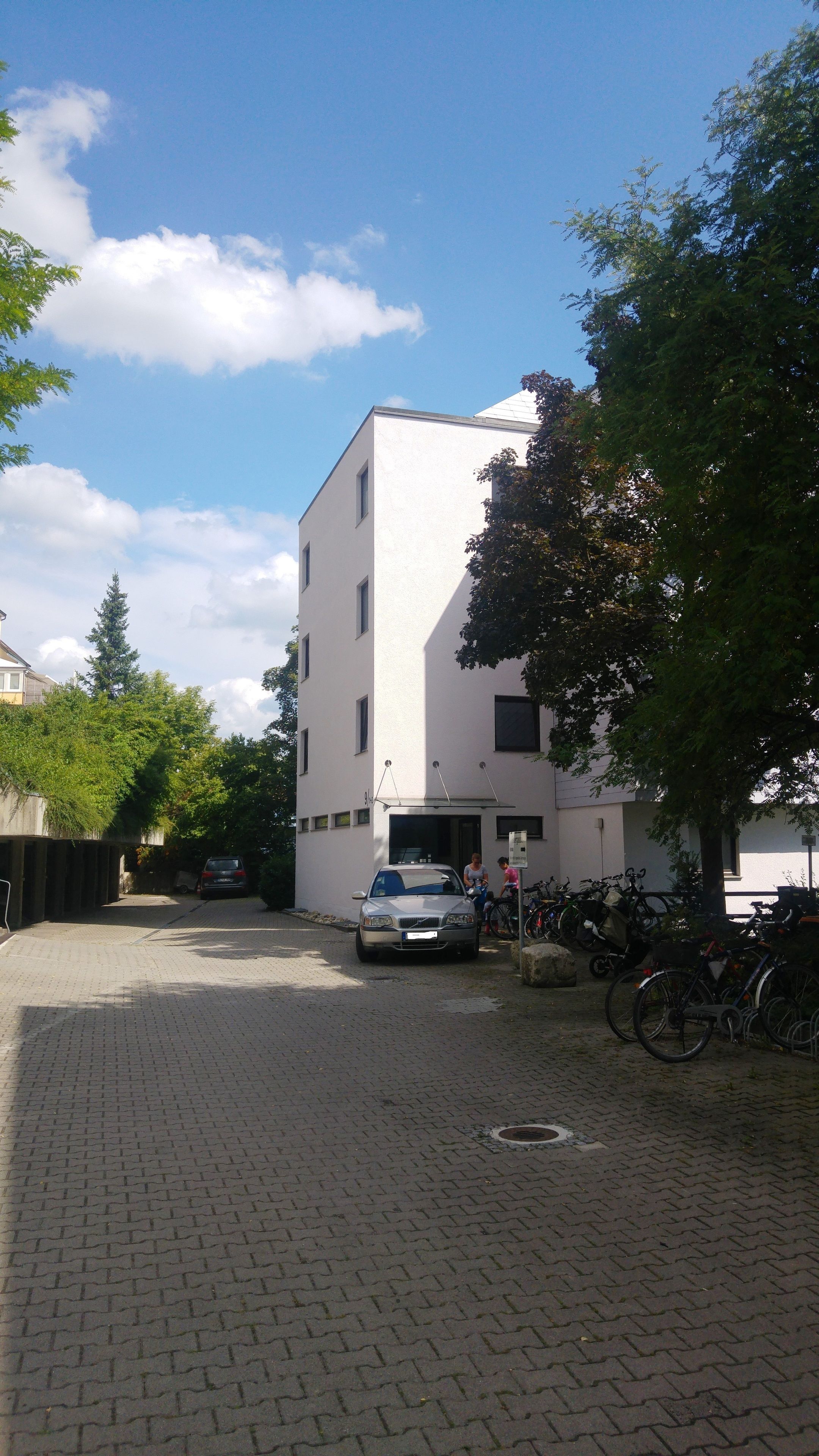 A building with a white facade, a paved courtyard, and bicycles parked outside.