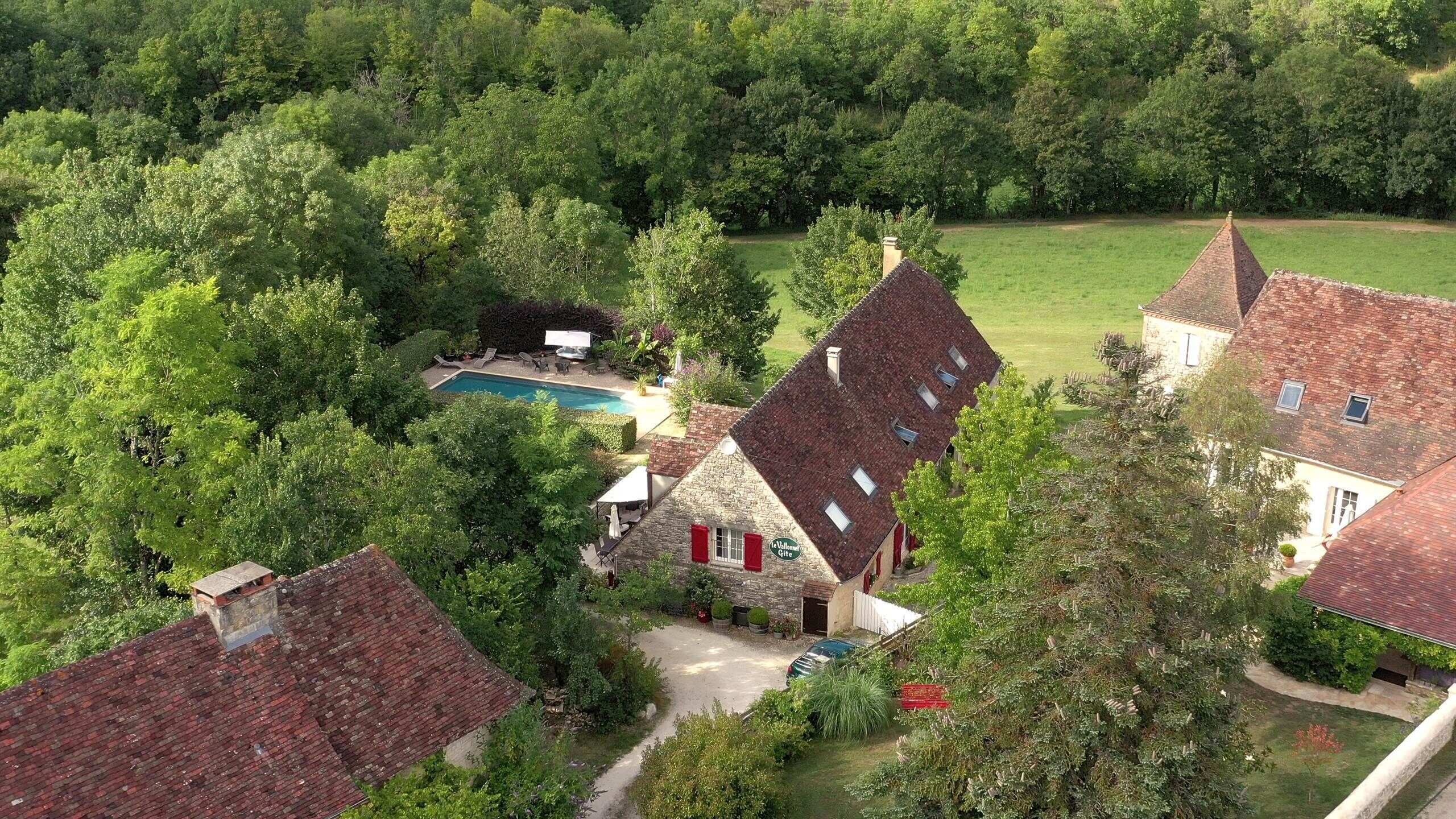 Vue aérienne d’une propriété dotée d’une piscine, de bâtiments en pierre et d’un environnement verdoyant.