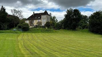 A stone house with a sloped roof, surrounded by a well-maintained lawn and dense trees.