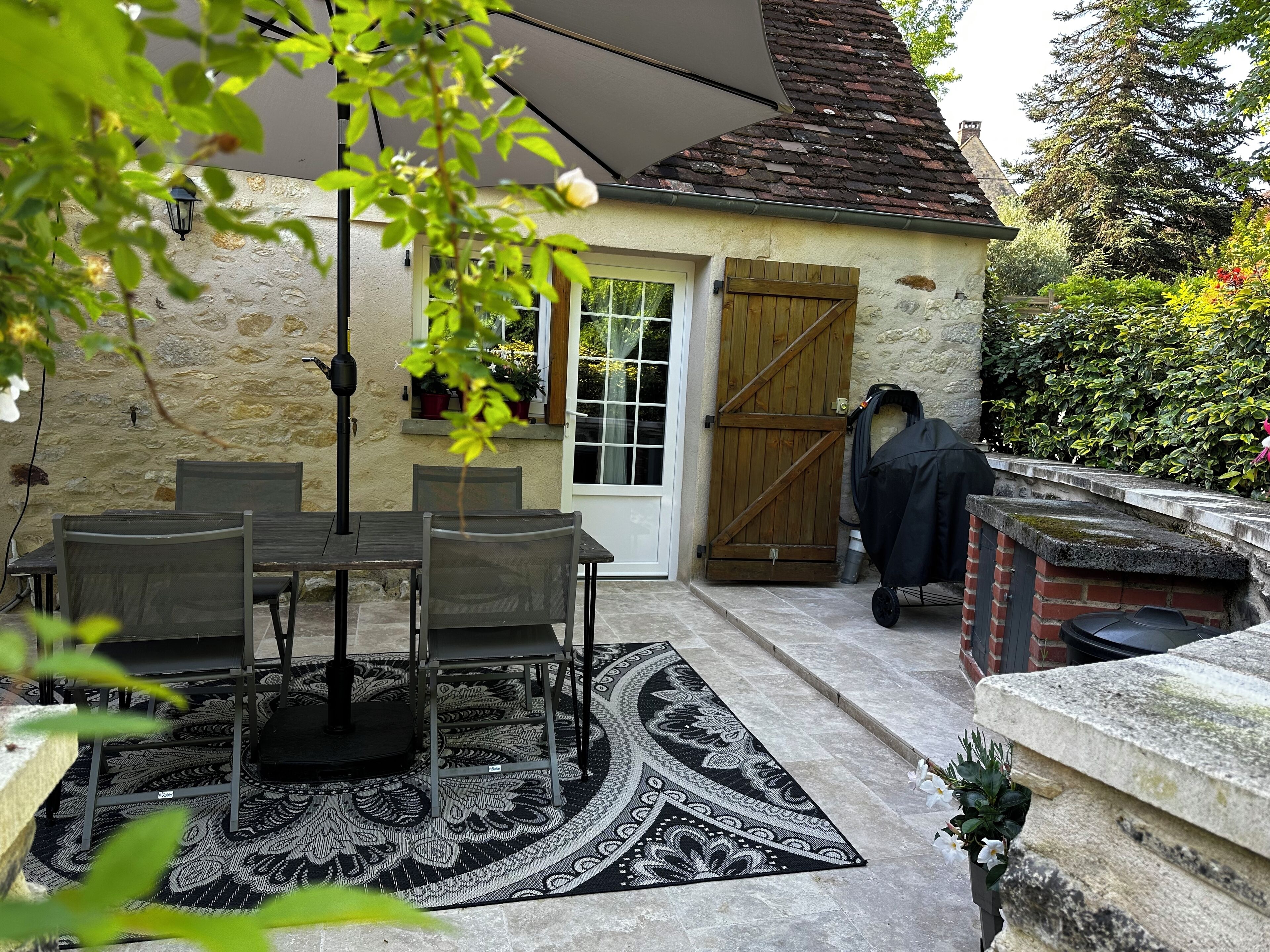 Un patio con mesa y sillas, un tapete estampado, una puerta de madera y una parrilla para barbacoa.