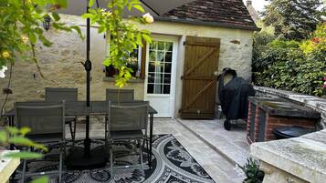 Un patio con mesa y sillas, un tapete estampado, una puerta de madera y una parrilla para barbacoa.