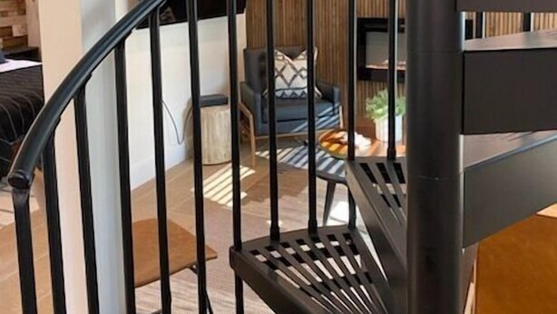 Una escalera moderna con barandilla de metal negro que lleva a una sala de estar con televisor de pantalla plana, un sofá y una mesa de centro.
