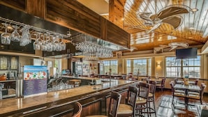 A spacious bar area with a high ceiling and wooden beams, featuring a bar counter, multiple seating areas, and a menu board. - Oceanfront Key Largo Paradise - Private Beach + Pool, Hot Tub & Marina (Tavernier)