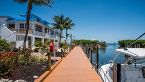 A wooden dock leading to a marina with boats, a white building with blue accents, and palm trees. - Oceanfront Key Largo Paradise - Private Beach + Pool, Hot Tub & Marina (Tavernier)