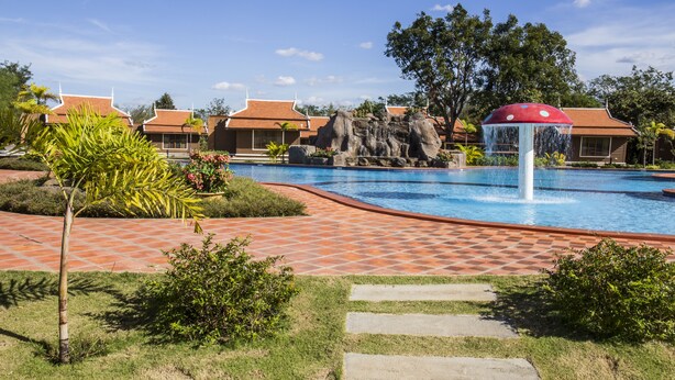 A swimming pool with a water fountain, surrounded by a tiled walkway and greenery. - Steung Chinet Bungalow (Santuk)