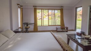 A hotel room with a large bed, a desk, a chair, and a view of the garden.