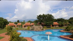 A swimming pool with a rock feature, surrounded by a brick pathway and palm trees. - Steung Chinet Bungalow (Santuk)