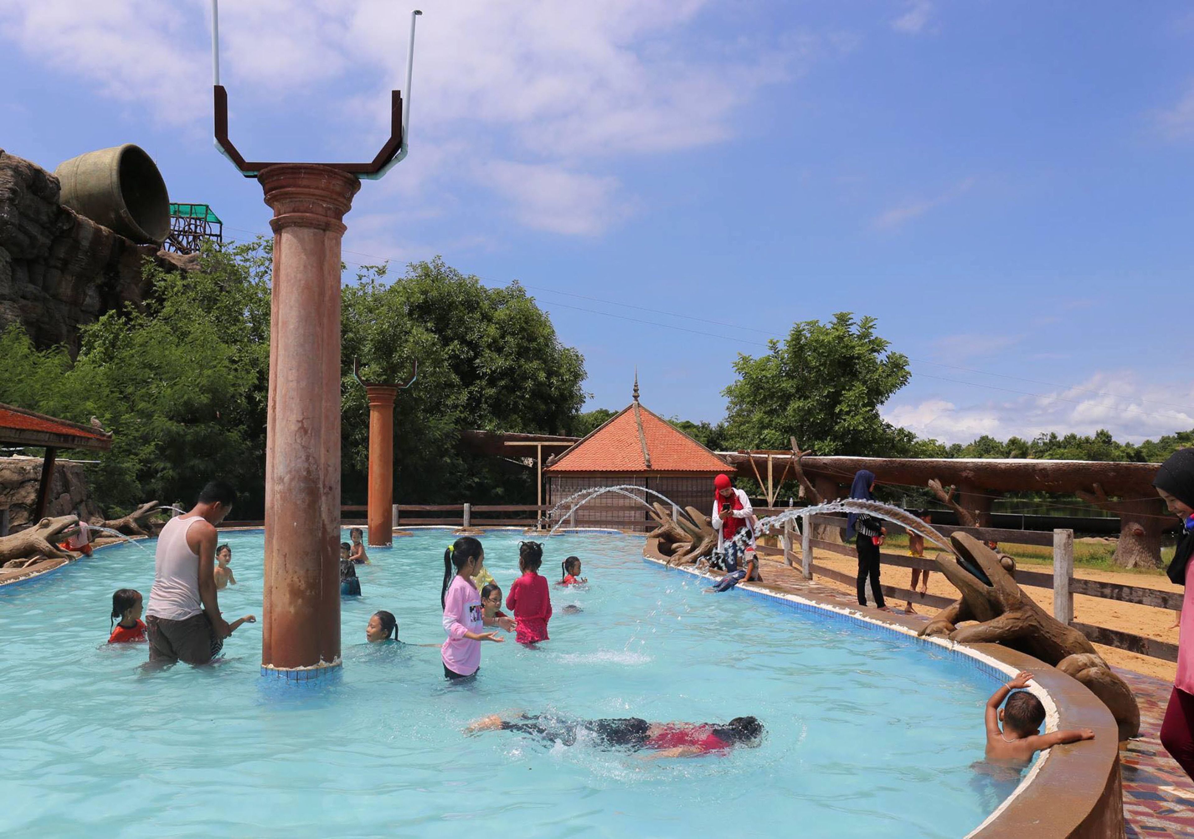 A swimming pool with a large central column, surrounded by people swimming and playing.