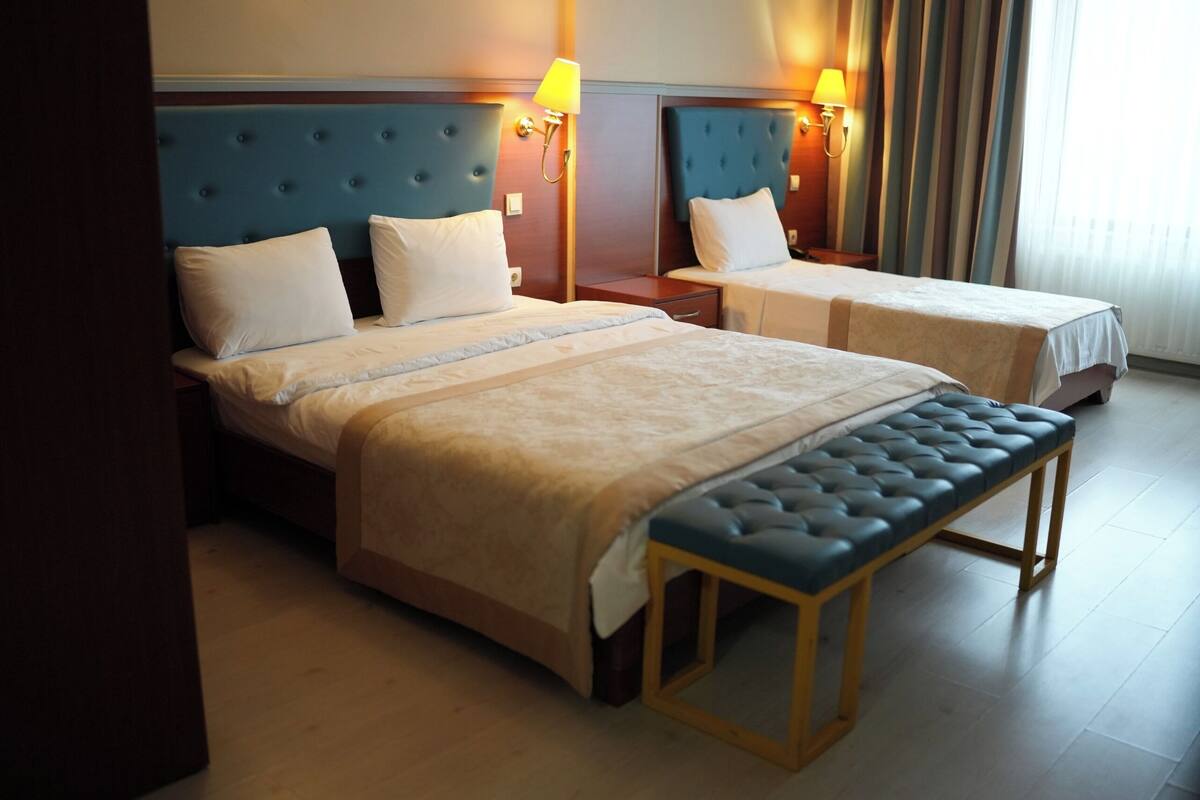 A hotel room with two beds, a bench, and a nightstand with lamps.