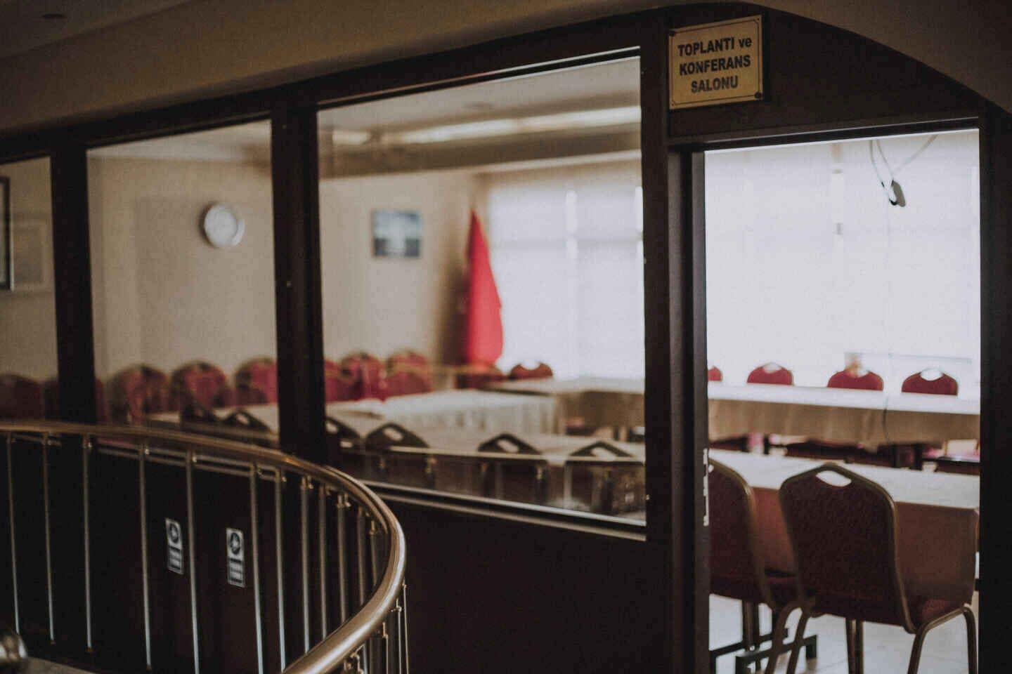 Une salle de conférence équipée de tables et de chaises, avec une horloge au mur et un panneau indiquant la fonction de la salle.