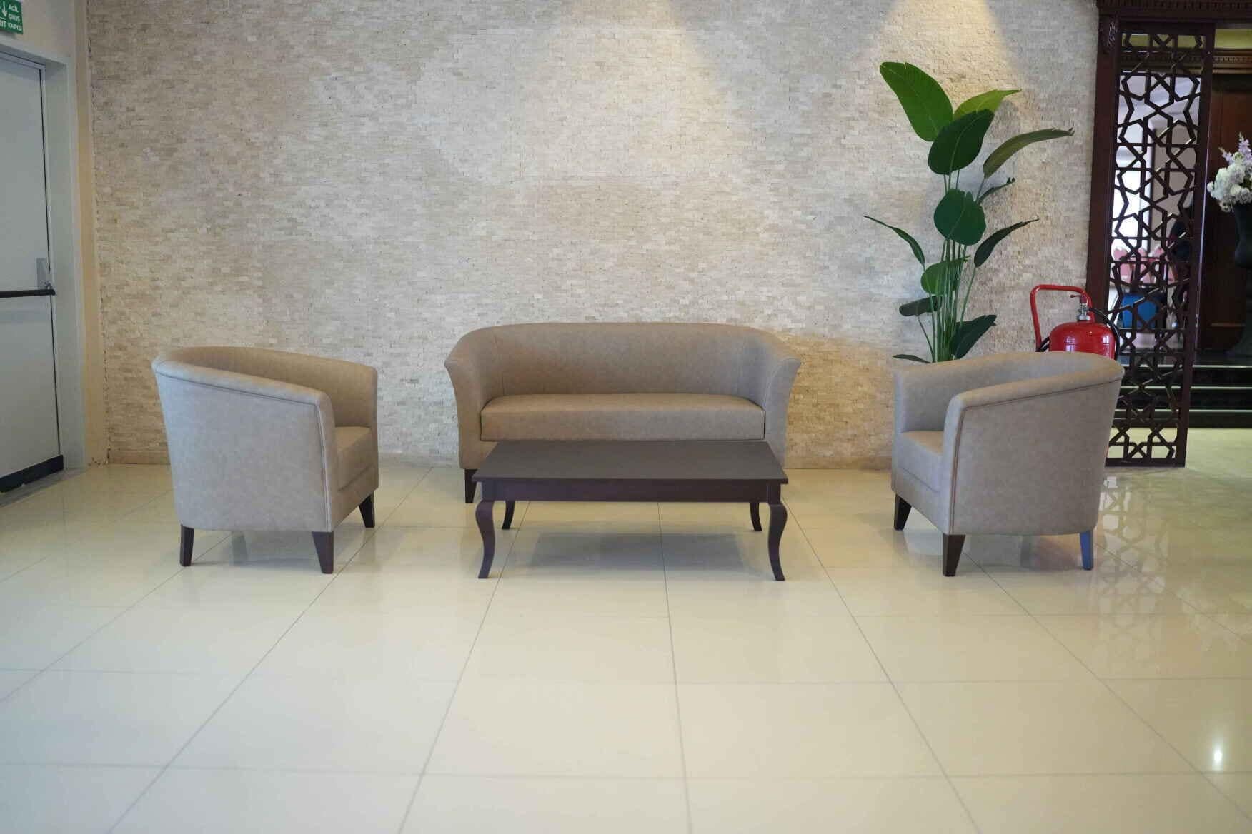 Un área de descanso con tres sillones y una mesa de centro en un vestíbulo con piso de baldosas y pared con textura.