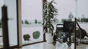 Una silla de ruedas en una habitación con un ventanal grande, una planta en maceta y vistas a un paisaje nevado.