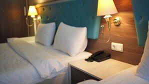 Una habitación de hotel con cama, lámparas de noche, teléfono y cabecero de madera.