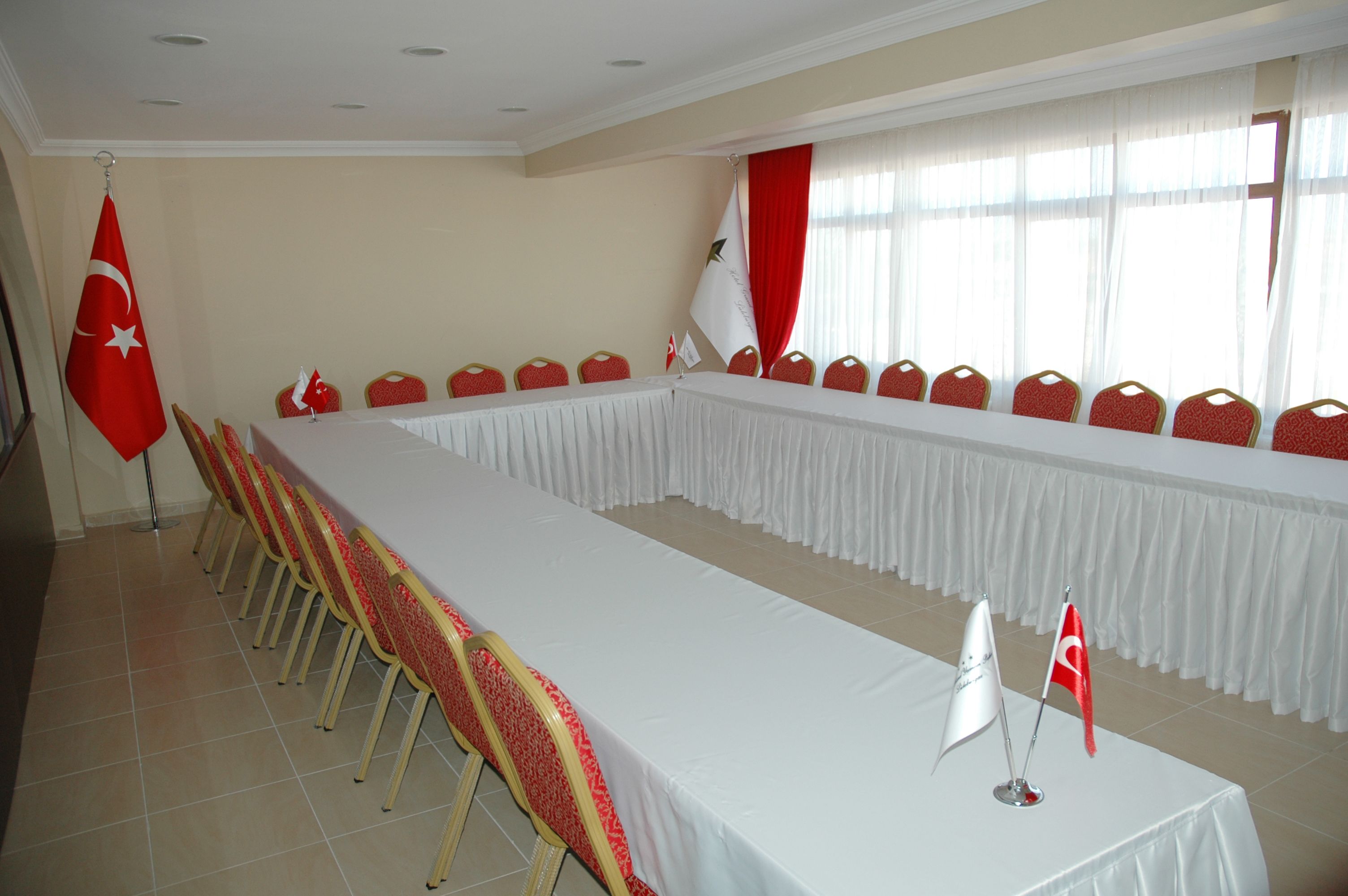 Un salón de conferencias con una larga mesa, sillas rojas y banderas.