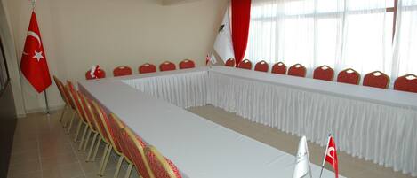 Un salón de conferencias con una larga mesa, sillas rojas y banderas.