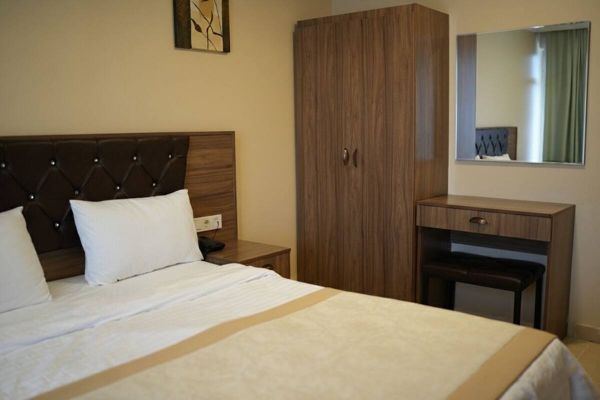 A hotel room with a large bed, a wooden wardrobe, a desk, and a mirror.