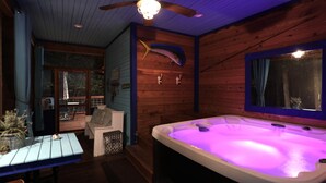 A wooden cabin interior with a hot tub, wooden walls, a ceiling fan, and a view through a window. - Holly Hill Secluded Retreat 7 acrs, Perfect 2 Bedroom, Hot Tub, Pets (Broken Bow)